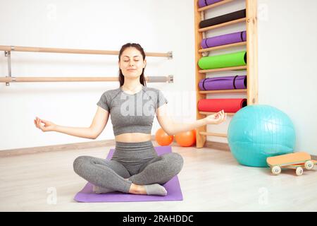 Das Mädchen macht Yoga-Übungen im Fitnessstudio, Gymnastik. Sitzt in Lotusposition auf der Matte. Stockfoto