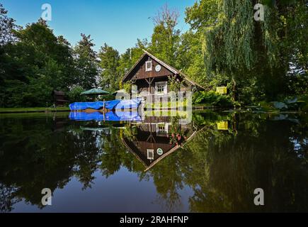04. Juli 2023, Brandenburg, Lübben: Die Morgensonne scheint auf ein kleines Holzhaus am Hafen der Stadt Lübben im Spreewald. Ein Spreewaldkahn ist immer noch mit einer blauen Plane bedeckt. Am Dienstag erwarten die Menschen in Berlin und Brandenburg Wind und Wolken. Nach Angaben des Deutschen Wetterdienstes (DWD) beginnt der Tag bewölkt, im Norden Brandenburgs anfangs noch sehr bewölkt. Tagsüber bleibt er größtenteils trocken, zwischen Prignitz und Uckermark findet gegen Mittag ein individueller Schauer statt. Außerdem gibt es lokale Windböen, laut DWD gibt es eine kleine Chance Stockfoto