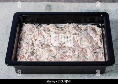 Italienischer Salat auf grauem Hintergrund. Salat mit Erbsen, Karotten, Kartoffeln, Salami, Gurken und Mayonnaise. Gesunde Vorspeisen Stockfoto