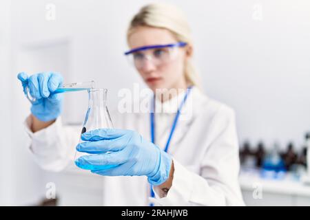 Junge blonde Wissenschaftlerin, die im Labor Flüssigkeit auf das Reagenzglas gießt Stockfoto