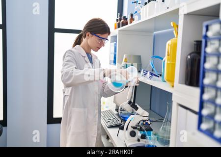 Junge blonde Wissenschaftlerin, die im Labor Flüssigkeit auf das Reagenzglas gießt Stockfoto