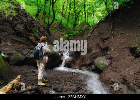 Ein Reisender an einem Wasserfall im Wald macht ein Foto mit einem Smartphone Stockfoto