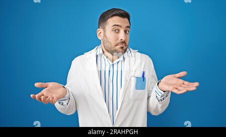 Junger hispanischer Arzt, ahnungslos über isolierten blauen Hintergrund Stockfoto