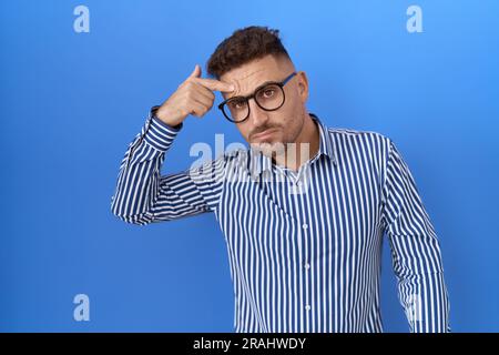 Lateinamerikanischer Mann mit Bart und Brille, der unglücklich auf die Stirn zeigt, hässliche Infektion von Schwarzkopf. Akne und Hautproblem Stockfoto