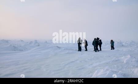 Weitwinkelblick auf eine kleine Gruppe von Touristen in einer gefrorenen arktischen Landschaft, die zwischen Hügeln von Schnee- und Eisformationen steht. Stockfoto