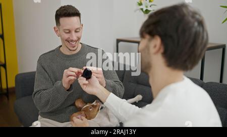 Zwei Männer lächeln zuversichtlich und überraschen zu Hause mit einem Verlobungsvorschlag Stockfoto