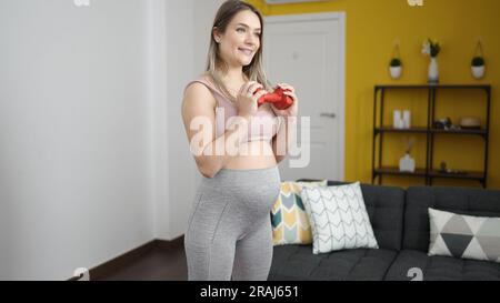 Junge schwangere Frau, die zuversichtlich lächelt und zu Hause die Kurzhantel hält Stockfoto