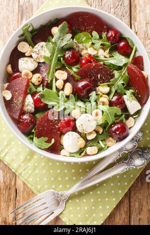 Frischer Sommersalat aus Rucola, gebackene Rüben, Kirschen, Mozzarella, Haselnüsse, Nahaufnahme in einer Schüssel auf dem Tisch. Vertikale Draufsicht von oben Stockfoto