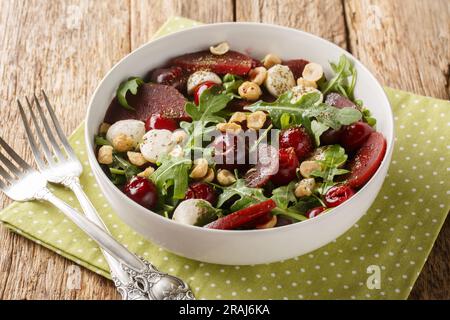 Diätetischer Gemüsesalat mit Rucola, Rüben, Kirschbeeren, Käse, Haselnüssen, Nahaufnahme in einer Schüssel auf dem Tisch. Horizontal Stockfoto