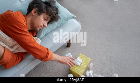 Kranker Mann mit Fieber, der zu Hause auf der Couch liegt, leidet an Schnupfen Grippe-Krankheit Niesen. Ein Typ fühlt sich schlecht Fieber Virus Symptome Stockfoto