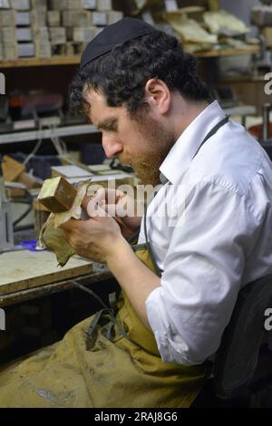 Ein chassidischer Handwerker formt Leder, während er Tefillin in seiner Kellerwerkstatt in Brooklyn, New York, herstellt Stockfoto