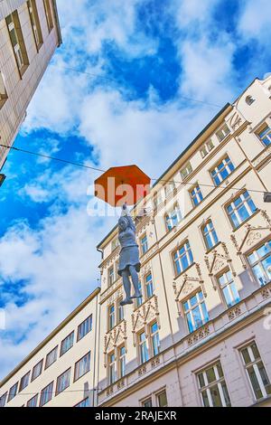 PRAG, TSCHECHIEN - 5. MÄRZ 2022: Hängende Regenschirmfrau oder leichte Ungewissheit Installation von Michal Trpak gegen das Haus und den blauen Himmel, am 5. März Stockfoto