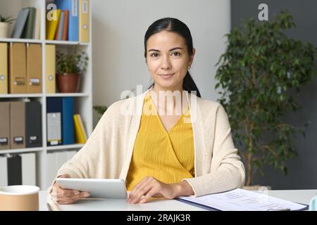 Porträt einer jungen schwangeren Geschäftsfrau, die vor der Kamera sitzt und am Tablet-pc arbeitet Stockfoto