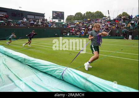 Das Bodenpersonal zieht die Regendecke heraus, während am zweiten Tag der Wimbledon-Meisterschaft 2023 im All England Lawn Tennis and Croquet Club in Wimbledon der Regen stoppt. Bilddatum: Dienstag, 4. Juli 2023. Stockfoto