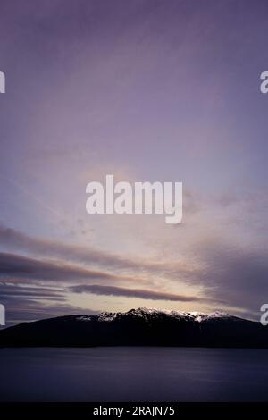 Abenddämmerung über schneebedeckten Bergen mit ruhigem Ozean Stockfoto