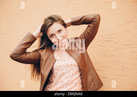 Außenporträt einer jungen Frau mit langen dunklen Haaren, die eine braune Lederjacke trägt Stockfoto