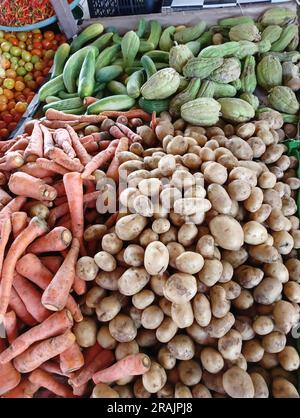 Blick aus einem hohen Winkel auf verschiedene frische Rohgemüse, einschließlich Kartoffeln, Karotten und Chayote, die an einem traditionellen Marktstand zum Verkauf angeboten werden. Stockfoto