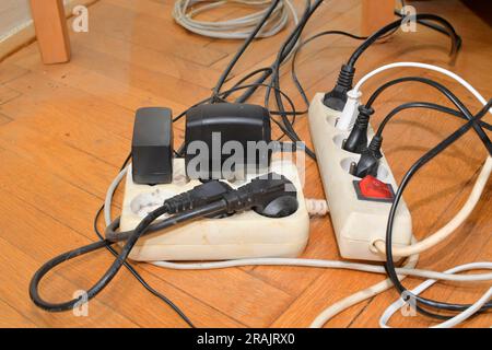 Verwickelte Kabel auf dem Parkettboden. Überlastete Schalttafeln auf dem Holzboden. Elektrische Kabel bei Störungen Stockfoto