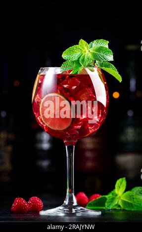 Alkoholische Cocktailgetränke aus königlicher Limonade mit Tequila, trockenem Gin, weißem Rum, Wodka, Likör, Limette, Himbeeren und Eis in Weinglas. Schwarzer Bartresen Ba Stockfoto