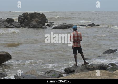 Modara, Colombo, Sri Lanka -August 05. 2022:Ein Sri-lankischer Fischer mit einer Holzstange fischt auf Felsen am Meer. Stockfoto