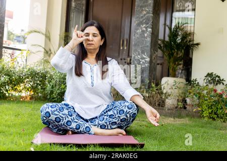 Indische, reife Frau, die Yoga im Garten macht Stockfoto