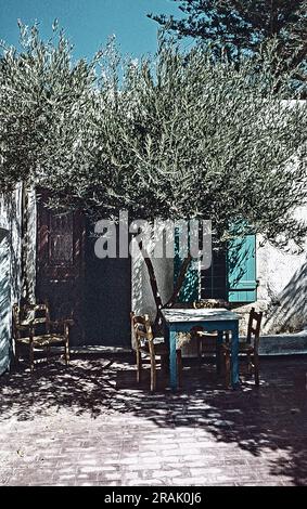 Generische Aufnahme als Fotografie, Tisch außerhalb des Eingangs im Schatten eines Baumes, wahrscheinlich Agia Galini, 1979 Stockfoto