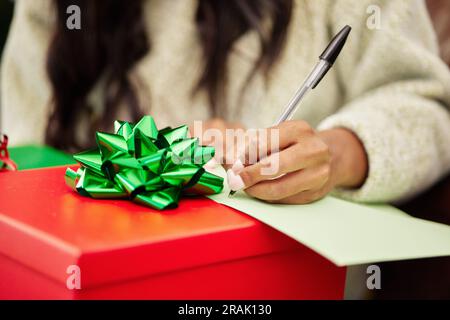 Frau, Hände und Schrift auf Weihnachtsgeschenk, Notiz oder Brief in Überraschung, Weihnachtszeit oder Dezember-Feiertag. Hand der Frau mit Stift und Papier Stockfoto