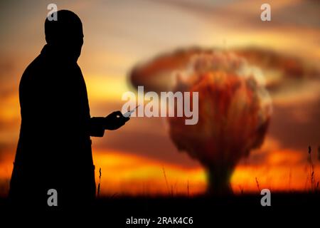 Das Konzept eines Atomstreiks. Silhouette eines Mannes mit einer Fernbedienung in den Händen, die eine Explosion verursacht. Ein Politiker, der einen Atomkrieg begann Stockfoto