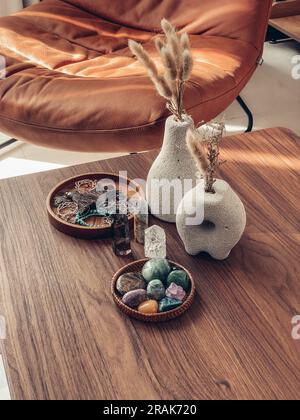 Dekorative Lavasteinvasen mit trockenen Blumen und heilenden Kristallen auf dem Tisch in der Wohnzimmerschließung Stockfoto