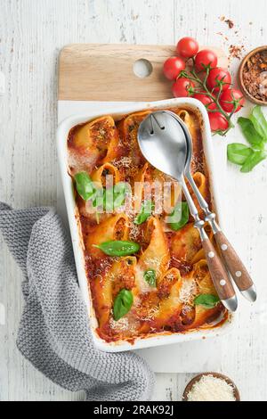 Cannelloni oder Conchiglioni. Gebackene gefüllte Nudelschalen mit Bolognese-Fleischsauce, Tomaten und Basilikum auf einem rustikalen weißen Holztisch. Traditioneller italienischer bo Stockfoto