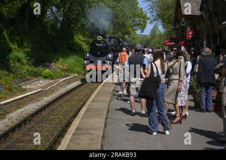 Leute (Eisenbahnbegeisterte), die den Zug loco 75078 beobachten, ankommen, rauchenden Rauch (nostalgische Fahrt mit der historischen Eisenbahn) - KWVR Haworth Station, England, Großbritannien. Stockfoto