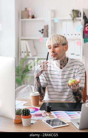 Tätowierter Grafikdesigner mit Apfel, der im Büro am Tisch arbeitet Stockfoto