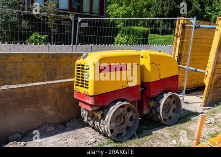 Kleine gelb-rote Bautrommelwalze zum Verdichten von Erde auf einer Baustelle. Seitenansicht. Stockfoto