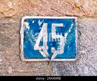 45 (fünfundvierzig) ein verbeultes Schild mit Hausnummer auf einer Steinmauer. Stockfoto