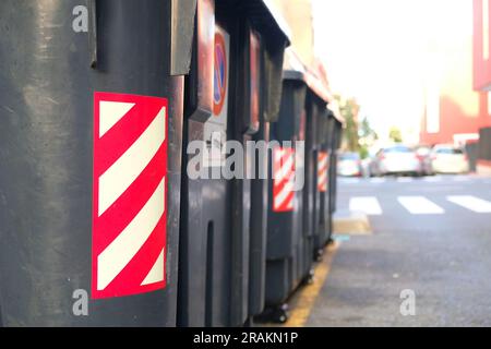 Schwarze Kunststoffabfallbehälter mit reflektierendem Klebeband, kommunale Abfallentsorgungseinrichtungen. Stockfoto