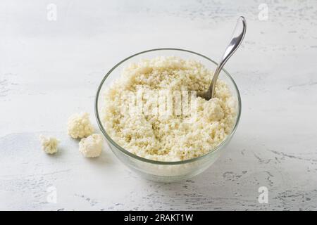 Geriebener Blumenkohl, Blumenkohl-Reis oder Blumenkohl-Couscous auf einem hellblauen Tisch. Kochen köstliches, veganisches, gesundes Essen. Stockfoto