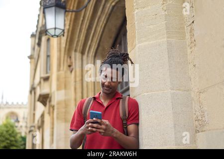 Männlicher Student, der Nachrichten oder soziale Medien auf einem Mobiltelefon außerhalb des Universitätsgebäudes in Oxford UK abfragt Stockfoto