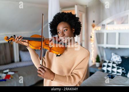 Eine attraktive junge afroamerikanische Musikerin spielt die Violine und praktiziert ein Musikinstrument Stockfoto