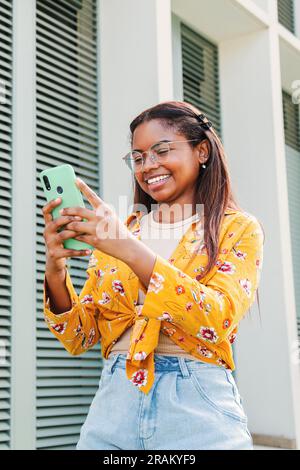 Vertikales Porträt einer jungen hispanischen glücklichen Frau, die mit einem Mobiltelefon im Internet surft. Lateinische Teenagerin, die Nachrichten in sozialen Medien mit einer Smartphone-App und drahtloser Technologie schickt. Hochwertiges Foto Stockfoto