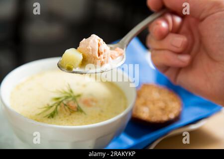 Eine Schüssel finnische Lohikeitto-Suppe, serviert auf einem Holztisch mit einem Stück schwedischem Roggenbrot. Cremige Brühe, zarte Kartoffeln und fleckiger rosa Lachs Stockfoto