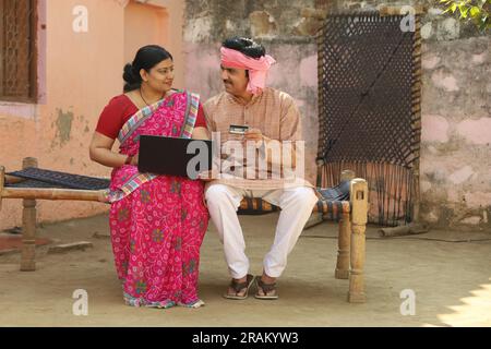 Eine glückliche Familie aus dem indischen Dorf, die den Laptop vor dem Haus benutzt hat. Mann und Frau zahlen gerne online mit Kreditkarte Stockfoto