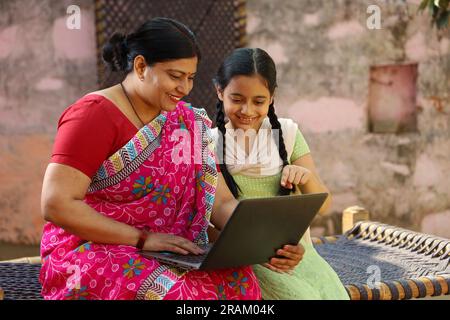 Eine glückliche Familie im indischen Dorf, alleinerziehende Mutter und Tochter, die ihren Laptop außerhalb des Hauses benutzen. Digitales Indien. Kindererziehung. Ermächtigung der Frau. Stockfoto