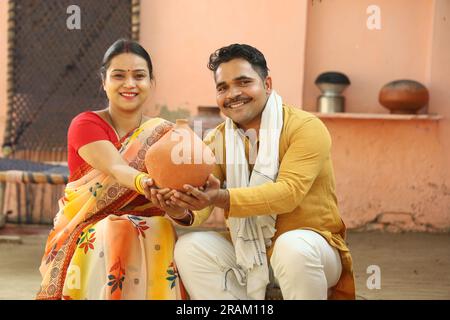 Glückliche, ländliche Indianerinnen in Saree, die mit ihrem Mann sitzen und Piggy Bank halten. Die Familie zeigt ihre Liebe zu ihrem gesparten Geld. Münze einlegen. Stockfoto