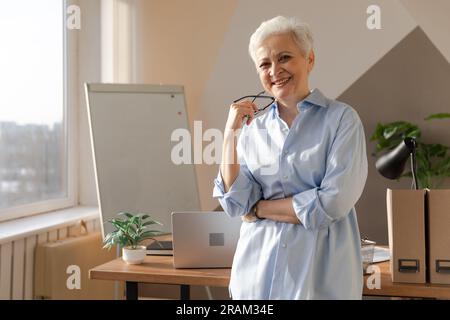 Portrait einer selbstbewussten, stilvollen europäischen Seniorin mittleren Alters am Arbeitsplatz. Stilvolle, ältere, 60s-jährige, grauhaarige Geschäftsfrau in einem modernen Büro. Chefführer Lehrer Berufsarbeiter Stockfoto