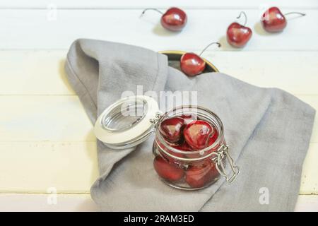 Ein kleiner, luftdichter Glasbehälter mit reifen Kirschen auf einem grauen Tuch Stockfoto