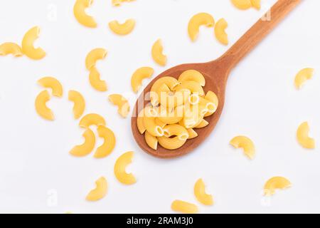 Ungekochte Chifferi Rigati Pasta in Holzlöffel auf weißem Hintergrund. Fett und ungesunde Lebensmittel. Verstreute Klassische Trockene Makkaroni. Italienische Kultur und Küche. Rohe Pasta Stockfoto