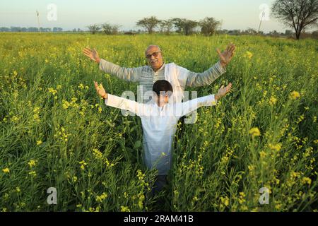 Ein junges, glückliches indisches älteres Bauernpaar, das mit seinem Enkel auf dem Senffeld steht und landwirtschaftliche Gewinne genießt. Ich bin froh, von den Ernten profitiert zu haben. Stockfoto