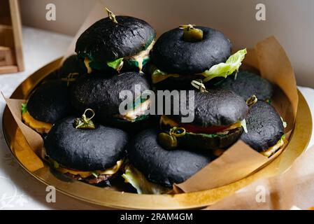 Köstliche Fast-Food-Burger mit schwarzem Teig, aufgespießt und garniert mit eingelegtem Cornichon und geschmolzenem Käse. Viele Portionen Fast-Food-Burger aus Stockfoto