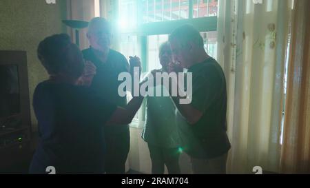Eine Gruppe von Senioren betet zu Hause zusammen mit Sonnenlicht, das durch das Fenster scheint. Vier verehrte ältere Menschen beteten, indem sie Hand an Hand hielten. Stockfoto