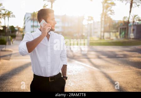 Selbstbewusster junger europäischer Geschäftsmann in formellen Outfits, der geschäftlich telefoniert, draußen steht, Kopierraum hat Stockfoto